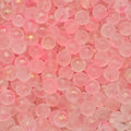 A close-up pile of small, round, translucent pink beads with a glossy finish and subtle gold glitter flecks.