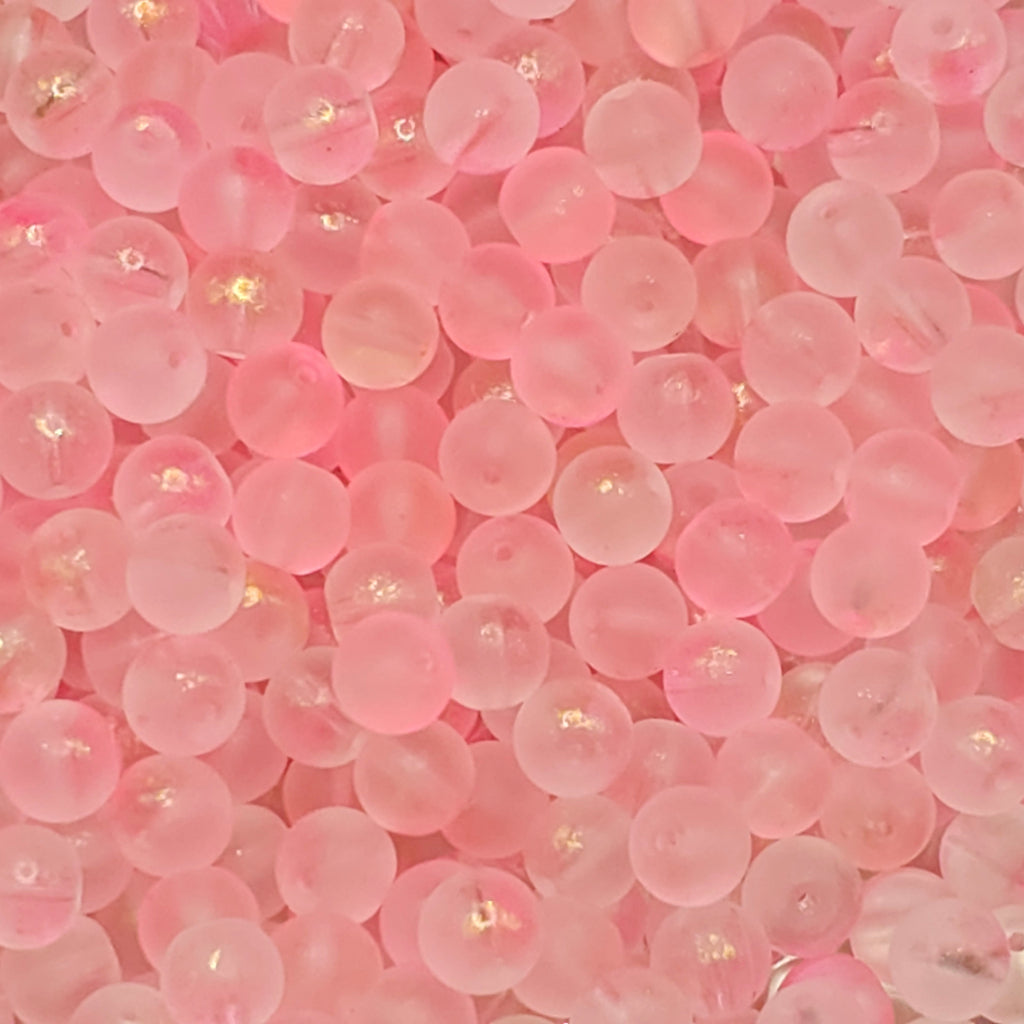 A close-up pile of small, round, translucent pink beads with a glossy finish and subtle gold glitter flecks.