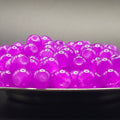 A close-up of glossy translucent purple boba pearls piled in a bowl against a dark gray background.