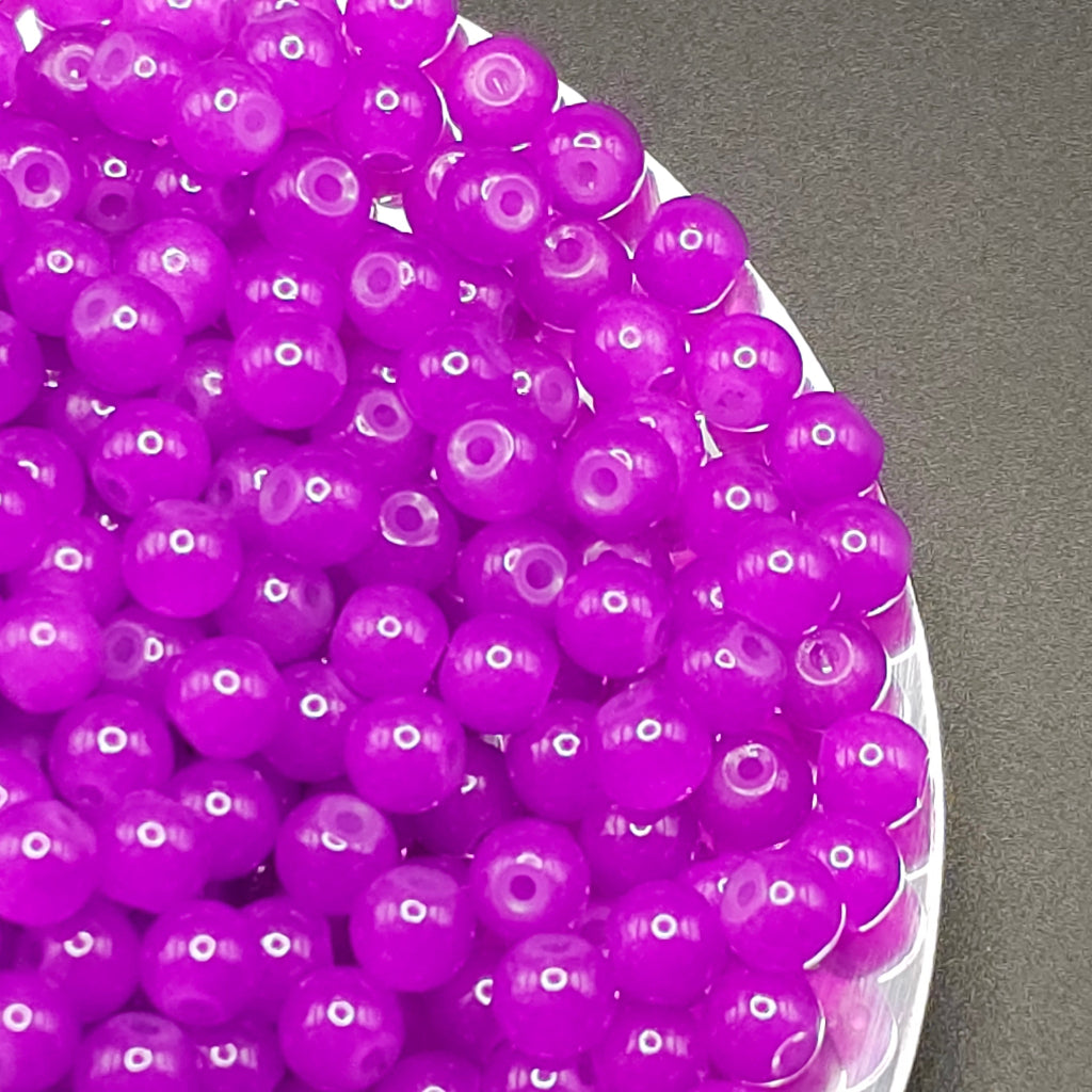 Bright purple plastic craft beads with hollow centers, piled on a white plate against a dark gray background.