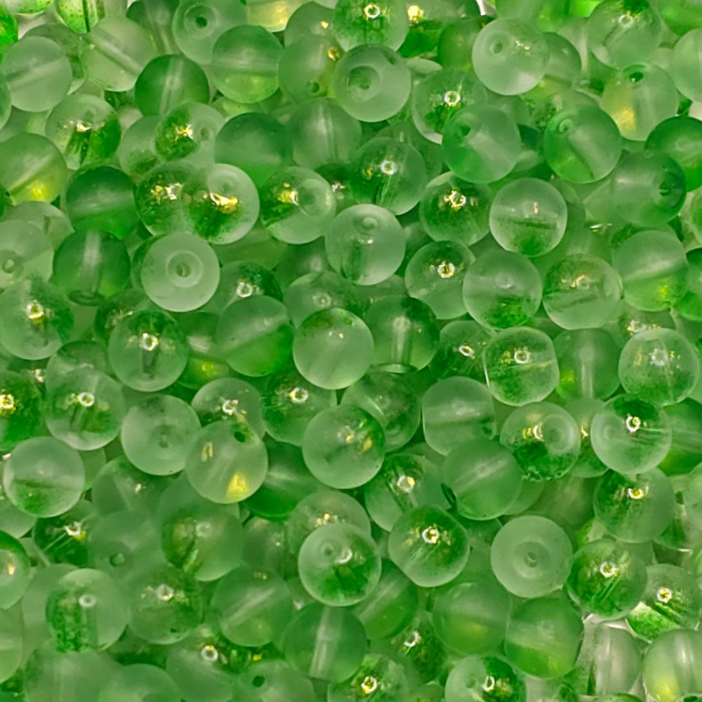 A close-up pile of translucent green glass beads with a frosted finish and small gold glitter flecks inside.