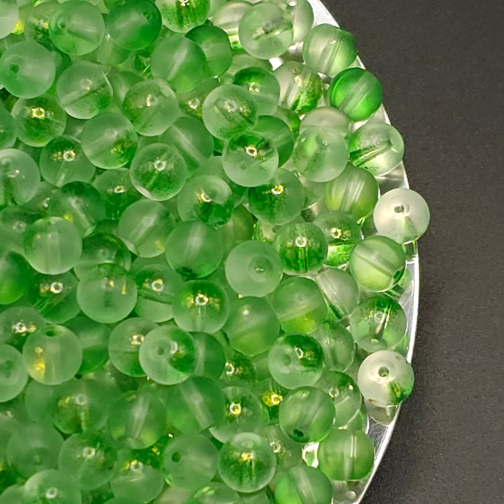 Green translucent round beads with small holes, piled on a silver tray against a dark gray background.