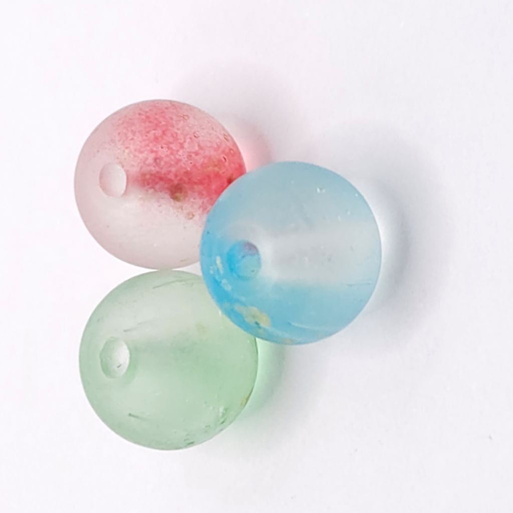 Three round translucent glass beads in pastel shades of mint green, light blue, and frosted pink with red speckling, arranged on a white background.