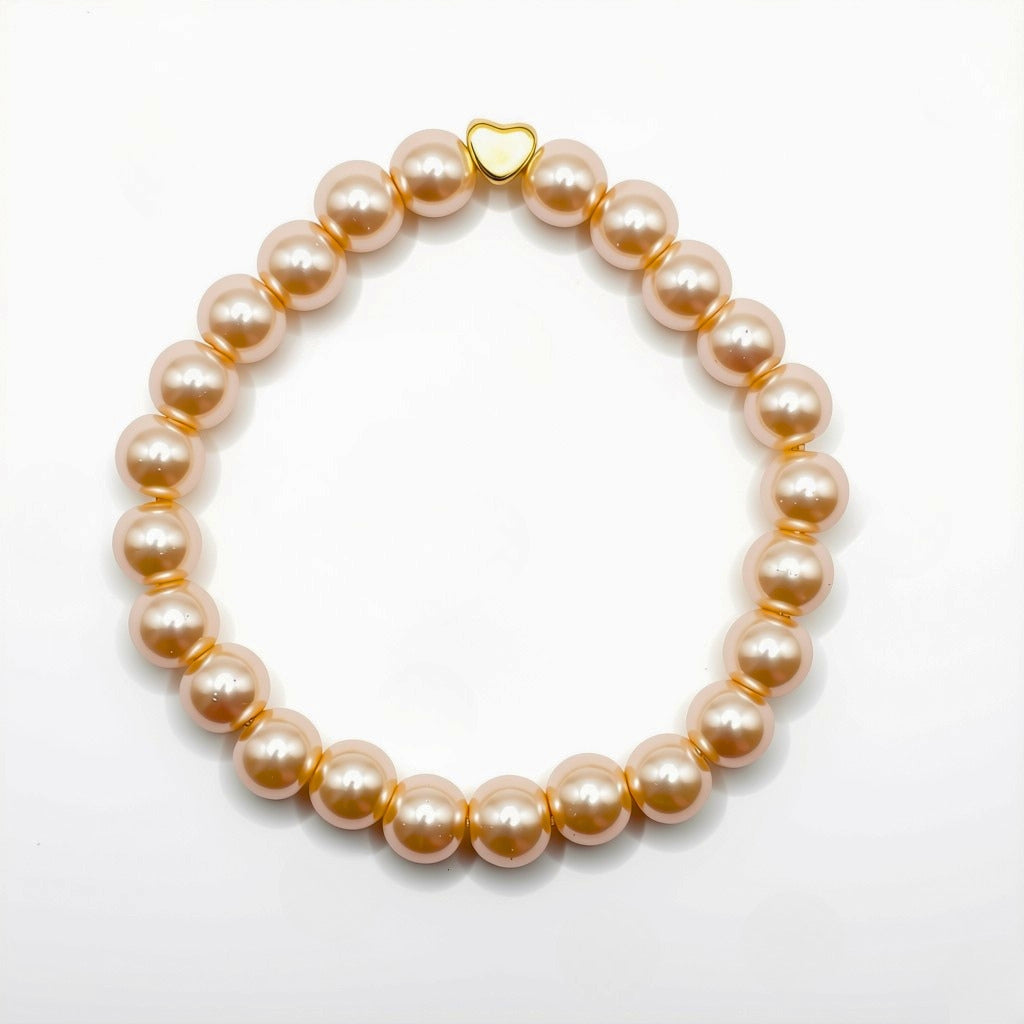 A caramel coloured pearlised glass bead bracelet with a small gold heart-shaped charm, photographed on a clean white background.