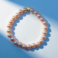 A pearlised bead bracelet with light beige beads and a small gold heart-shaped charm, photographed on a blue and white background with soft shadows.