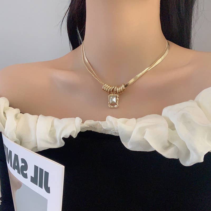 Model wearing a gold necklace with a clear gemstone on a plain background