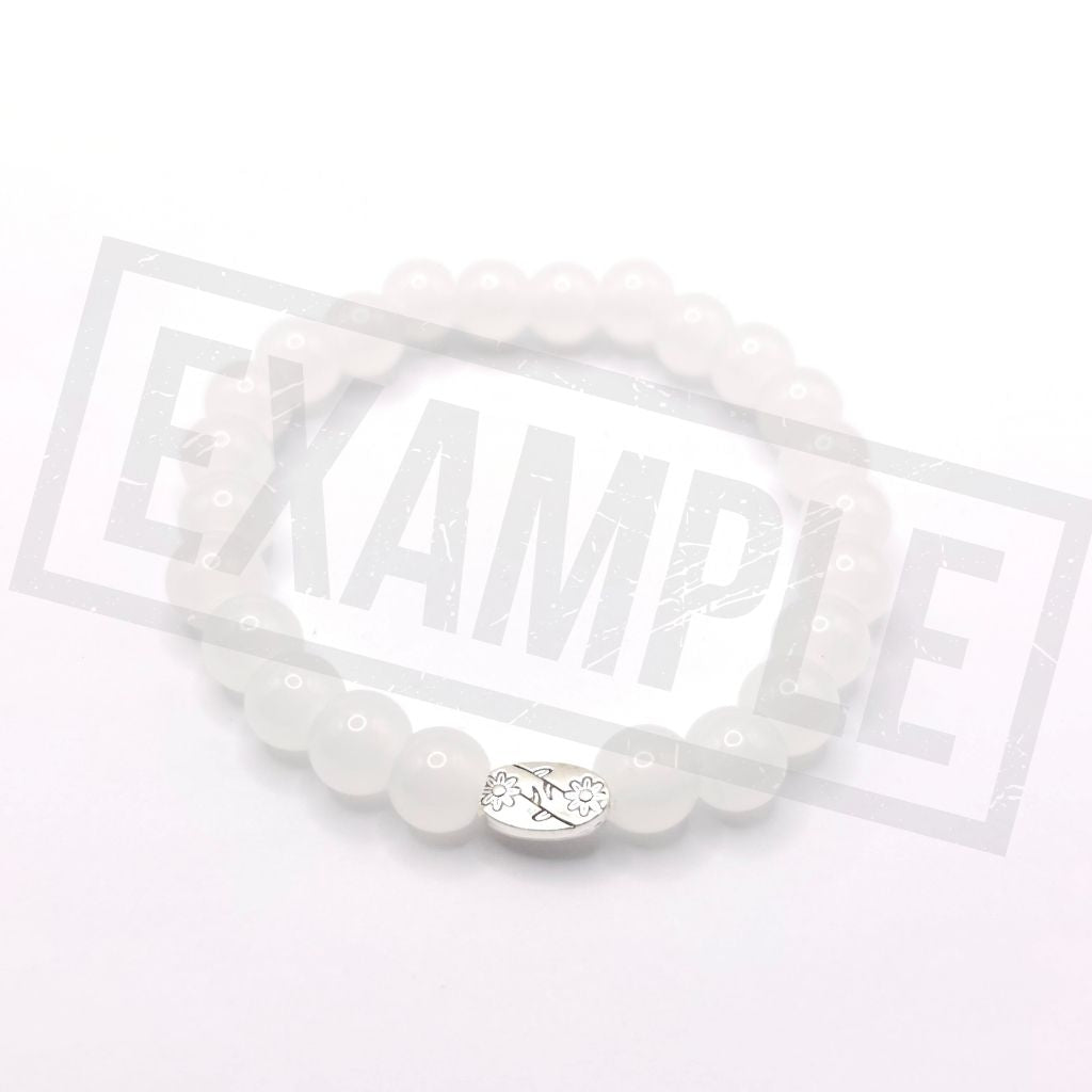 A moonstone white beaded bracelet with a silver oval charm featuring a floral design, displayed on a white background.