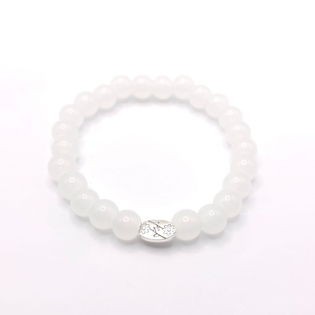 A white beaded stretch bracelet with a silver oval charm featuring a floral design, shown on a plain white background.