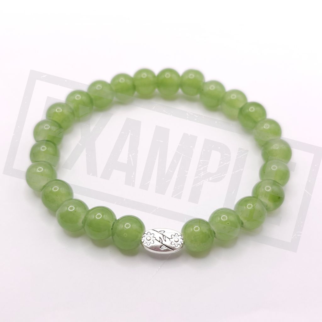 A olive green beaded stretch bracelet with a polished silver-toned oval charm featuring a floral pattern, displayed on a white background.