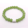 A green beaded stretch bracelet with a small silver-toned decorative charm, displayed on a clean white background.