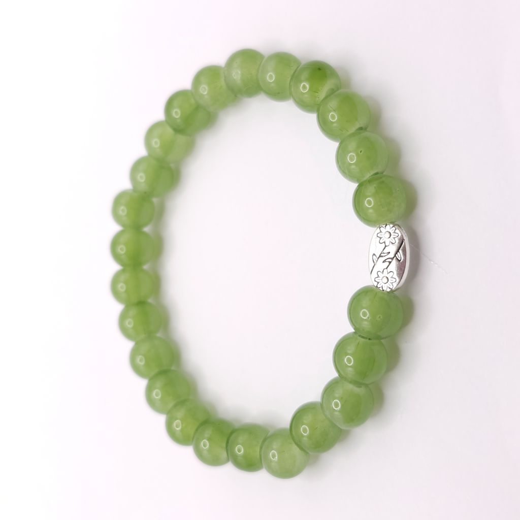 A green beaded stretch bracelet with a small silver-toned decorative charm, displayed on a clean white background.
