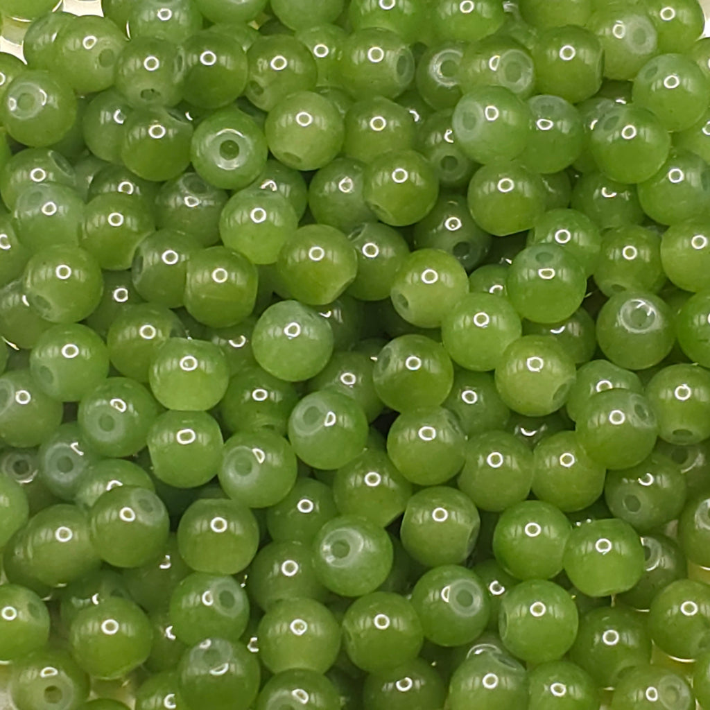 A close-up pile of small, round, translucent green beads with a central hole, showing a glossy finish and subtle highlights.