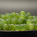 A close-up of glossy, translucent light green round beads with drilled holes, piled on a dark surface against a soft gray background.