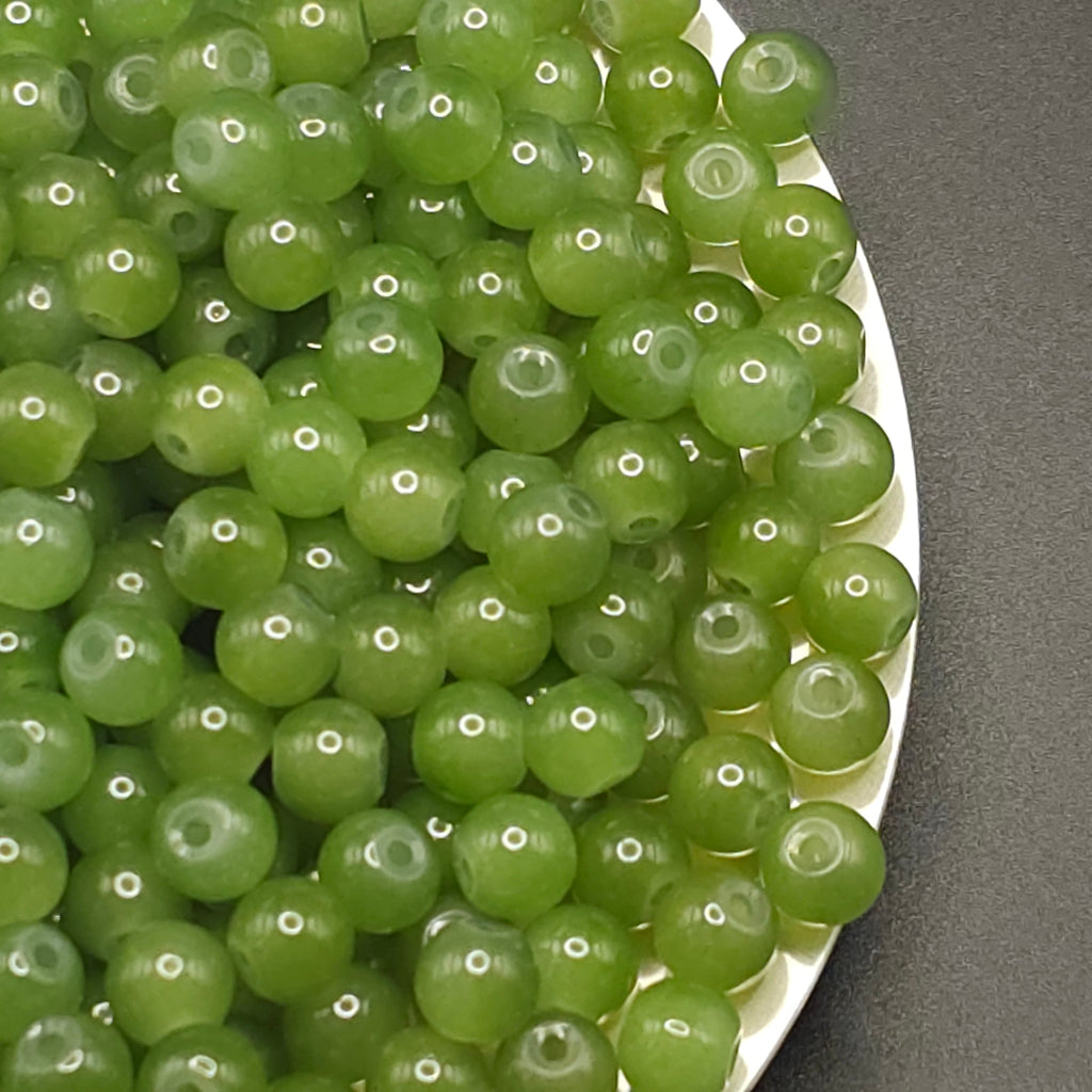 Green translucent round beads with drilled holes, piled on a white plate against a dark gray background.
