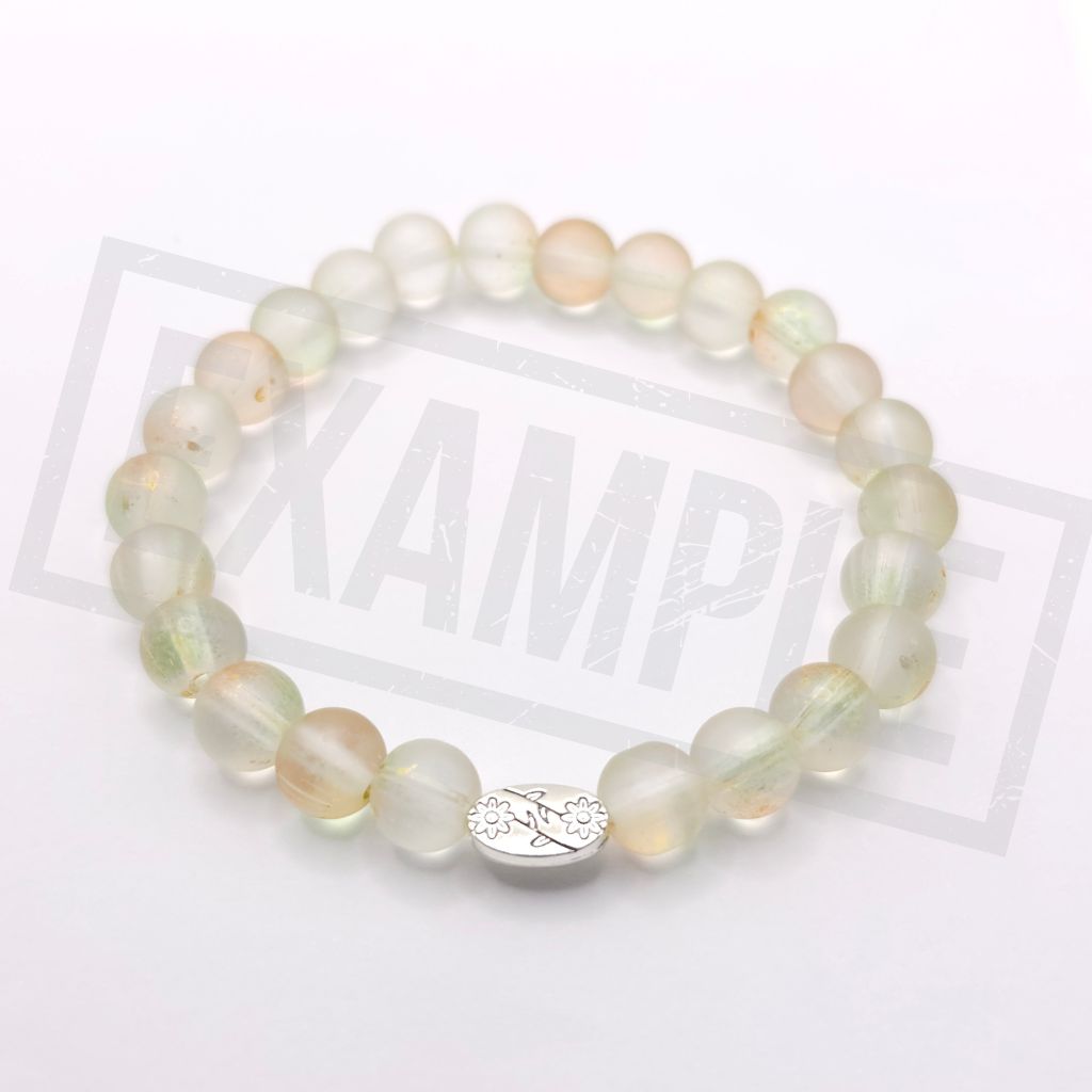 A beaded stretch bracelet made of pale translucent round beads with a small silver oval charm featuring a floral engraving, displayed on a white background.