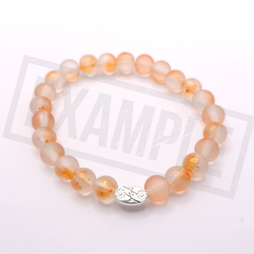 A beaded stretch bracelet made of translucent orange frosted beads, with a small silver oval charm featuring a floral design 