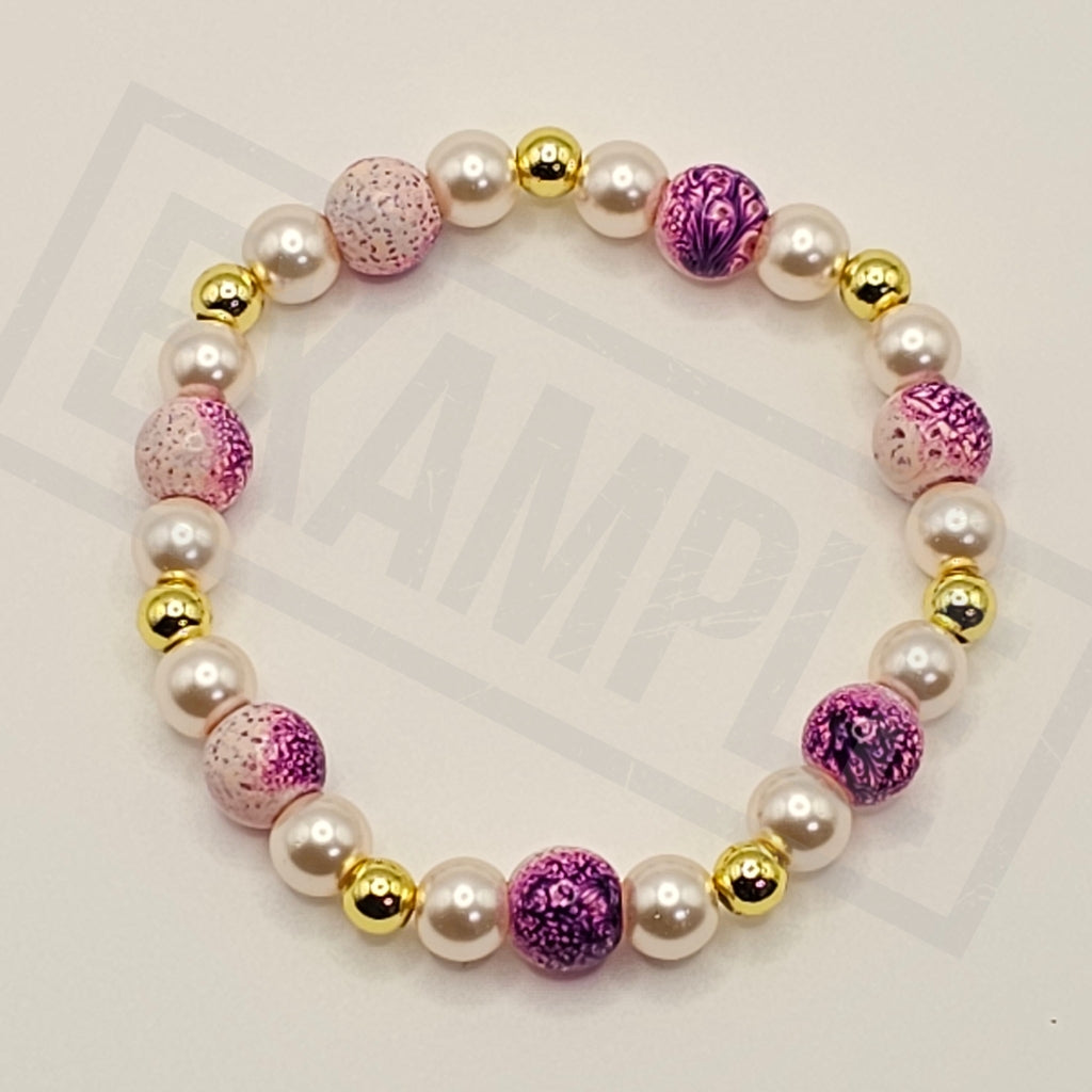 A beaded stretch bracelet featuring white faux pearls, metallic gold spacer beads, and alternating pink and purple marbled glass beads, displayed on a light gray background with a faint watermark.