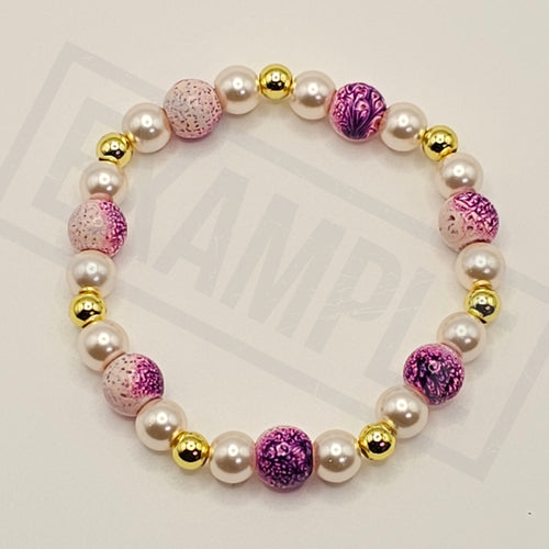 A beaded stretch bracelet featuring white faux pearls, metallic gold spacer beads, and alternating pink and purple marbled glass beads, displayed on a light gray background with a faint watermark.