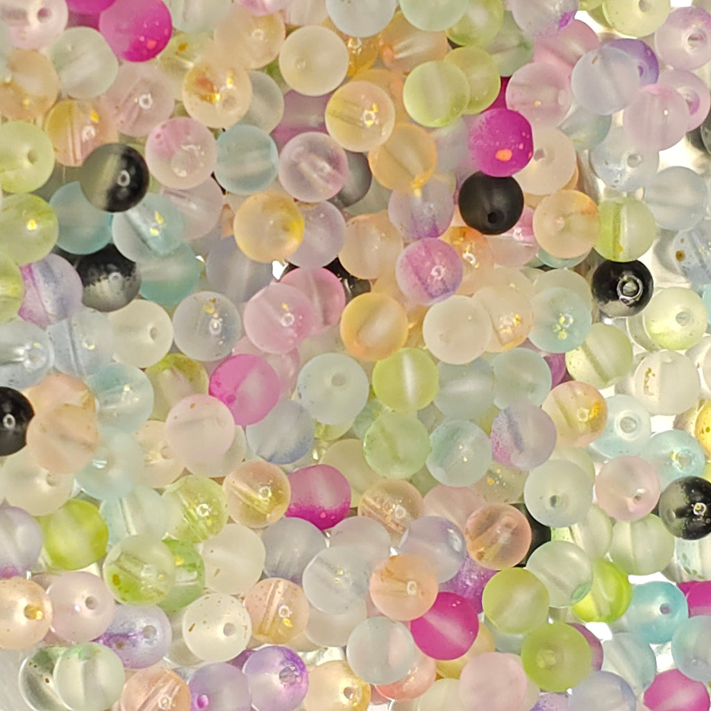 A close-up pile of small round translucent beads in pastel colors including pink, yellow, green, blue, purple, and some opaque black and white beads.
