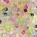 A close-up pile of small round translucent beads in pastel colors including pink, yellow, green, blue, purple, and some opaque black and white beads.