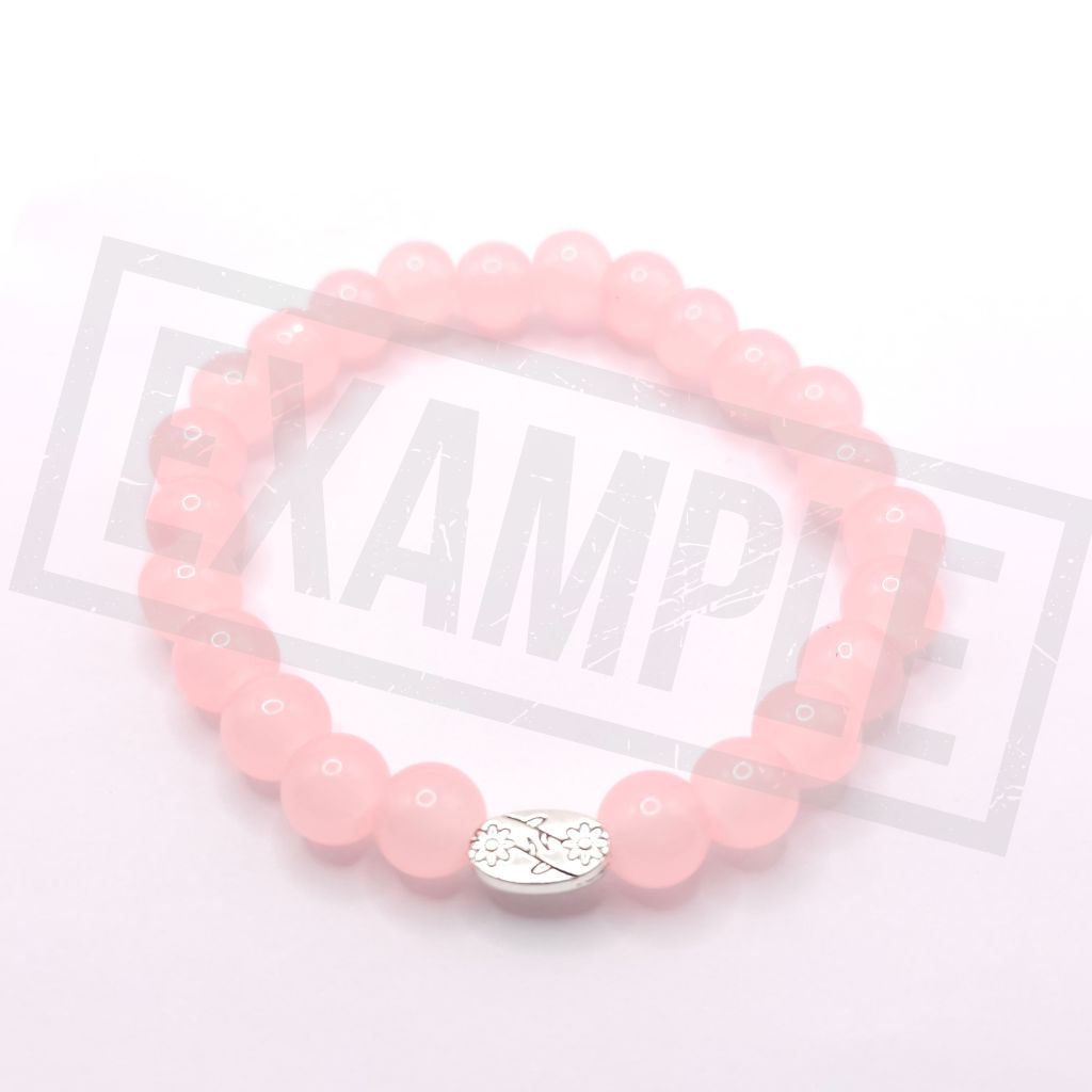 A peach beaded bracelet with a silver-toned oval charm featuring a floral design, displayed on a light pink background.