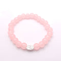 A pink beaded stretch bracelet with a small silver oval charm featuring a metal charm, displayed on a clean white background.