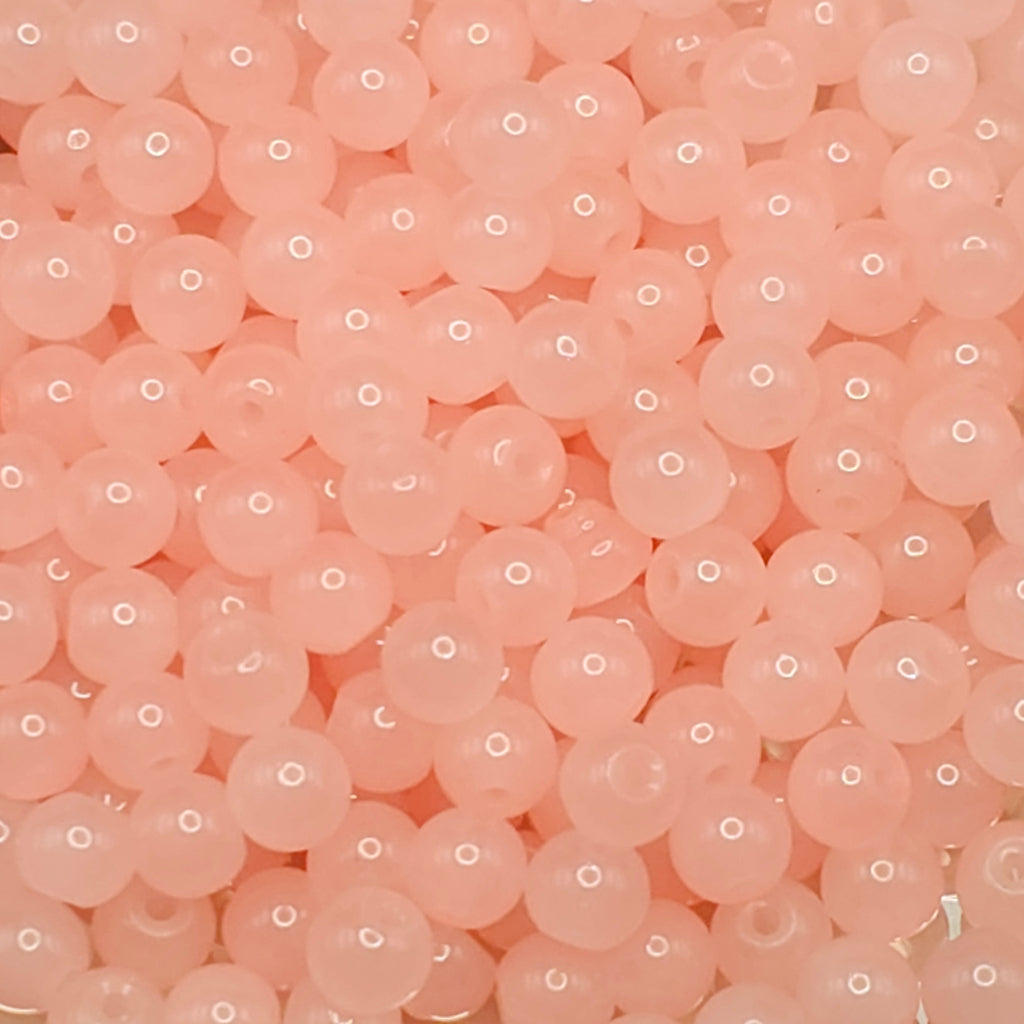 A close-up pile of small, round, translucent peach-pink beads with a glossy finish.