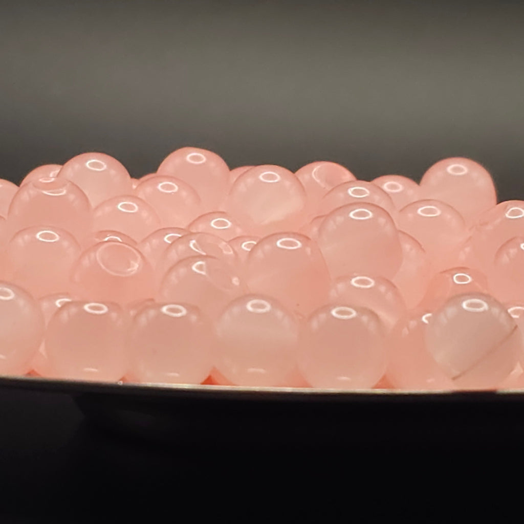 A close-up of many translucent pink gel beads or boba pearls piled in a shallow dish against a dark gray background.