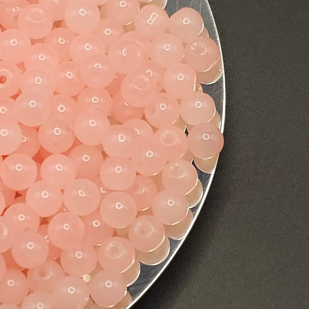 A close-up of many small translucent pink beads or boba pearls piled on a silver plate against a dark gray background.