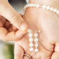 Pearl earrings being worn on a hand with a blurred background