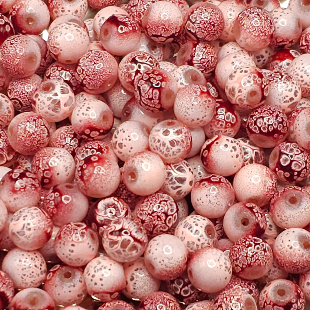 A close-up pile of round glass beads with a mottled pattern of deep red and pale pink, featuring white bubble-like speckles