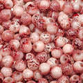 A close-up pile of round glass beads with a mottled pattern of deep red and pale pink, featuring white bubble-like speckles