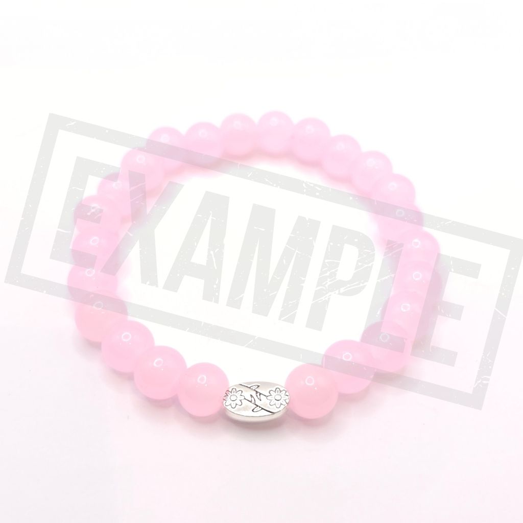 A pink beaded stretch bracelet with a silver oval charm engraved with small floral details, displayed on a white background.