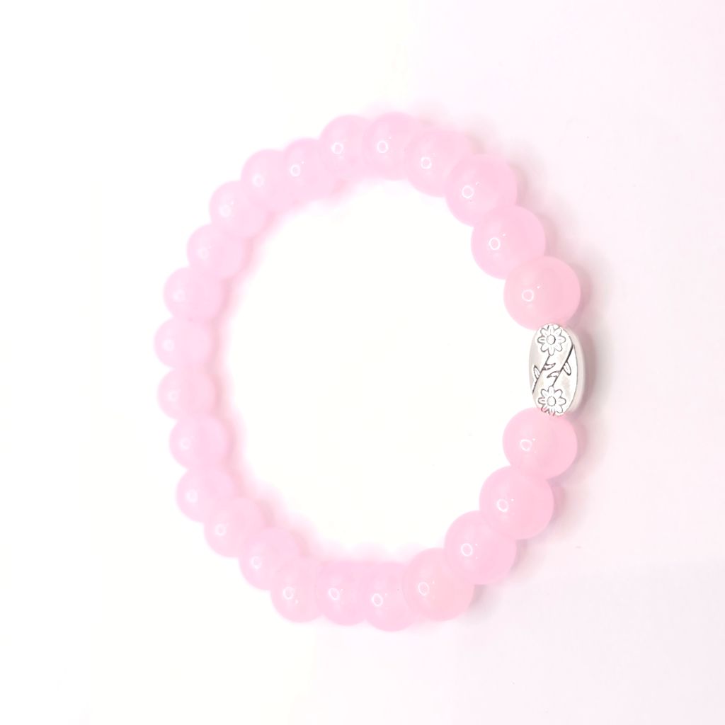A pink beaded stretch bracelet with a small silver oval charm featuring a floral design, displayed on a clean white background.