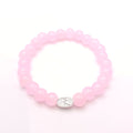 A pink beaded stretch bracelet with a small silver oval charm featuring a floral design, displayed on a clean white background.
