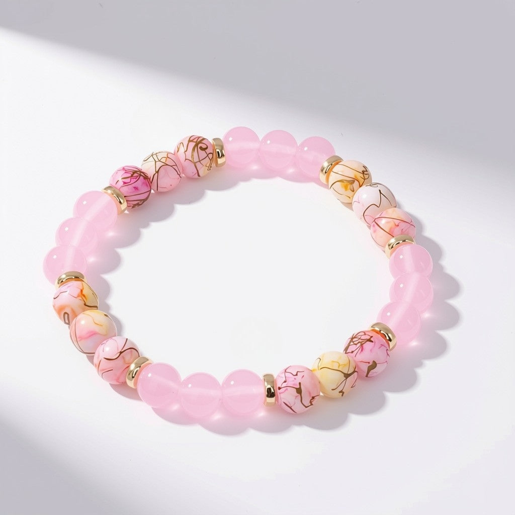 Pink translucent and marbled pink‑white‑yellow glass bead stretch bracelet with gold spacer rings arranged in a circle on a light background.