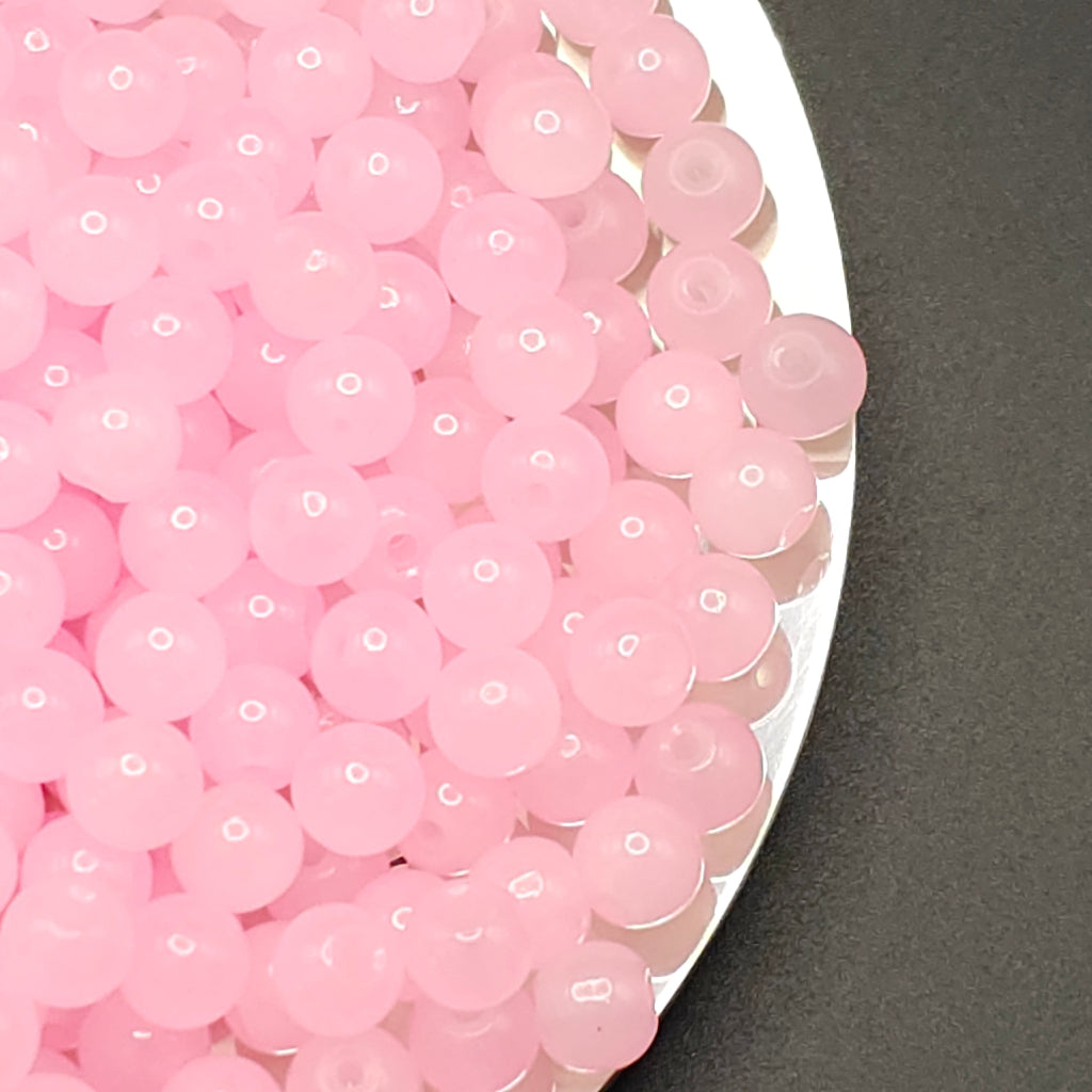 A close-up of many small translucent pink round beads or boba pearls piled on a white plate against a dark gray background.