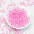 Pink translucent round beads scattered around and piled in a white scalloped dish on a light textured background.