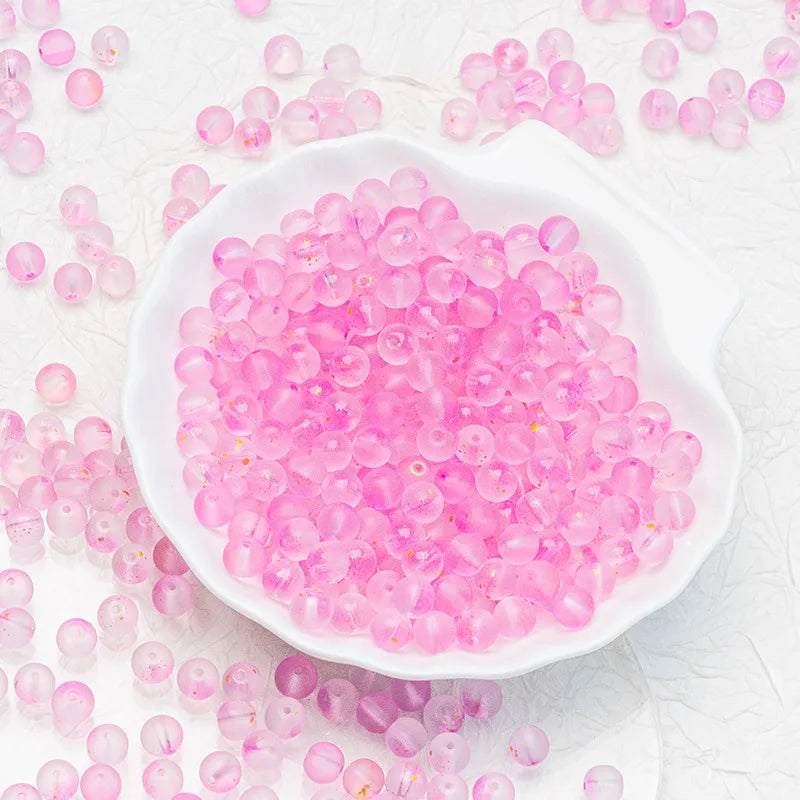 Pink translucent round beads scattered around and piled in a white scalloped dish on a light textured background.