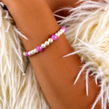 Bracelet with pink and white beads on a wrist against a fluffy white background
