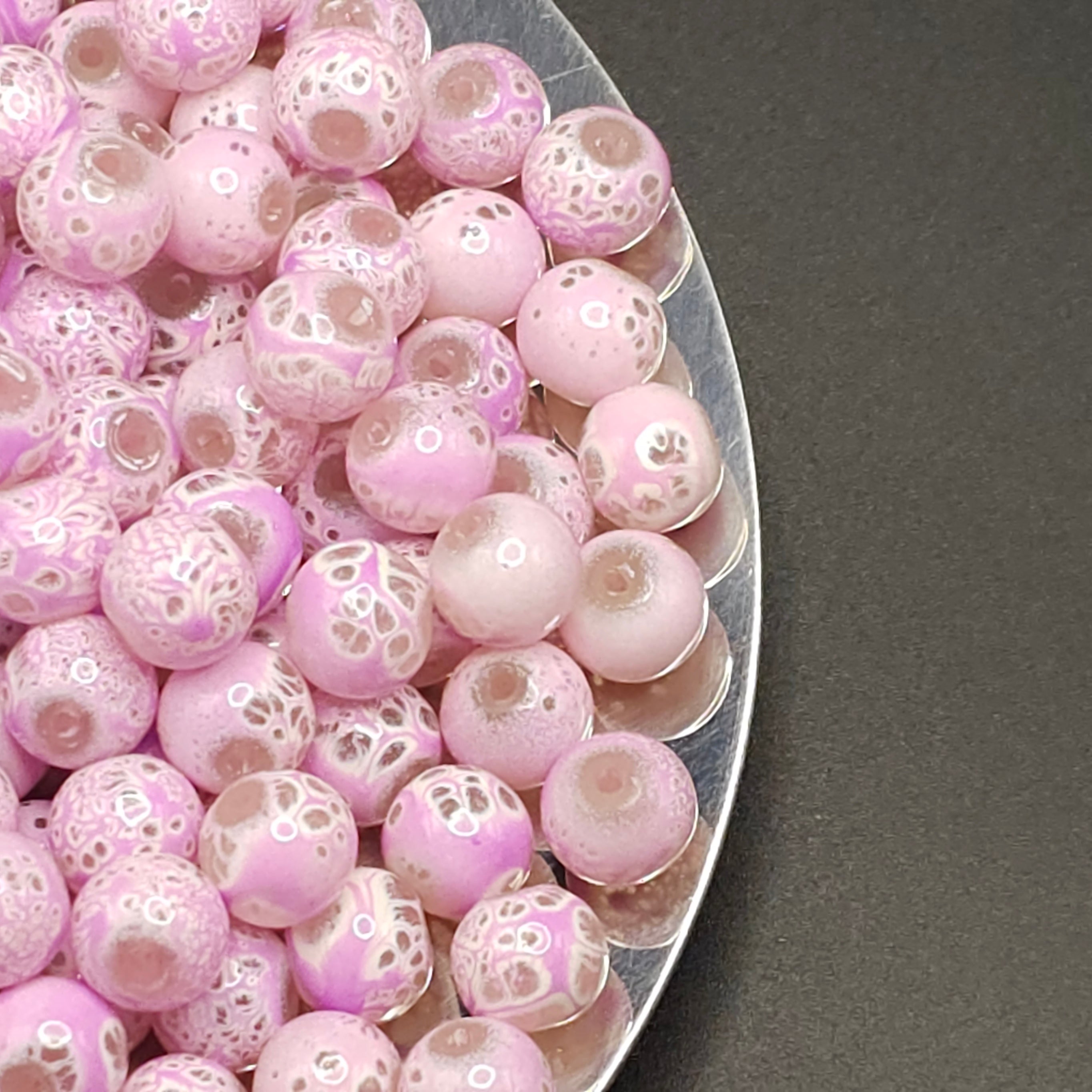 A pile of round glass lampwork beads in shades of Plum with white speckled patterns, displayed on a silver metal tray against a dark gray background.