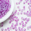 Purple translucent round beads scattered on a white textured surface with a white bowl partially visible on the left.
