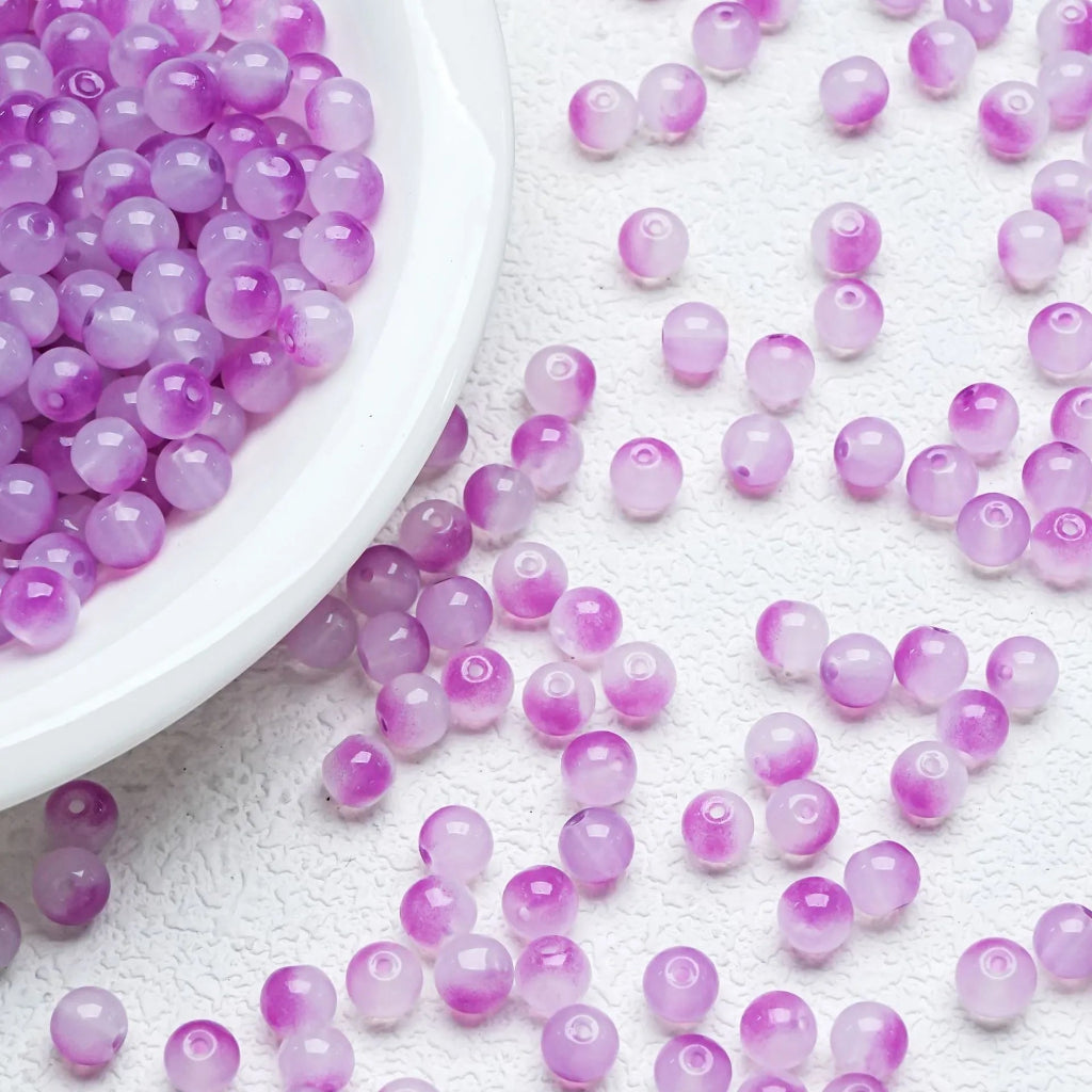 Purple translucent round beads scattered on a white textured surface with a white bowl partially visible on the left.