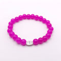 A beaded stretch bracelet made of bright magenta pink round beads, featuring a small silver oval charm in the center with a floral design.