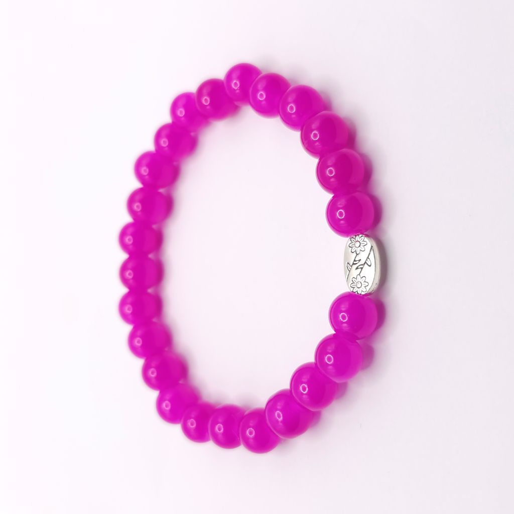 A beaded stretch bracelet made of bright magenta pink round beads, featuring a small silver oval charm in the center with a floral design.