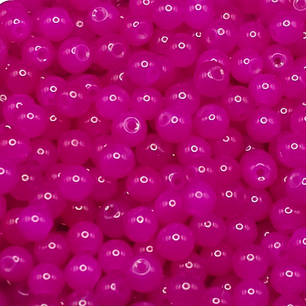A close-up pile of small, glossy, translucent magenta pink beads with white highlights.