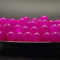 A close-up of glossy, translucent magenta pink boba pearls piled in a bowl, with a dark, out-of-focus background.