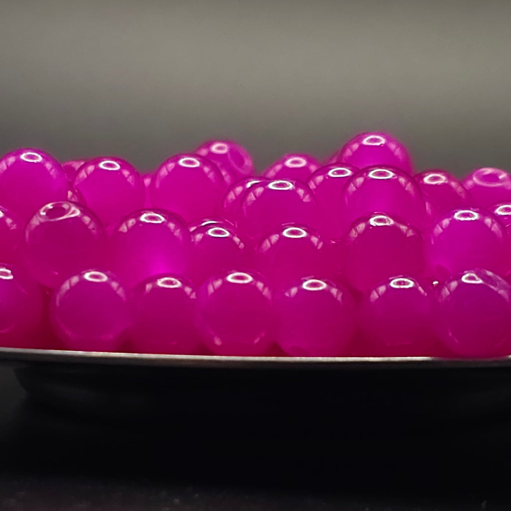 A close-up of glossy, translucent magenta pink boba pearls piled in a bowl, with a dark, out-of-focus background.