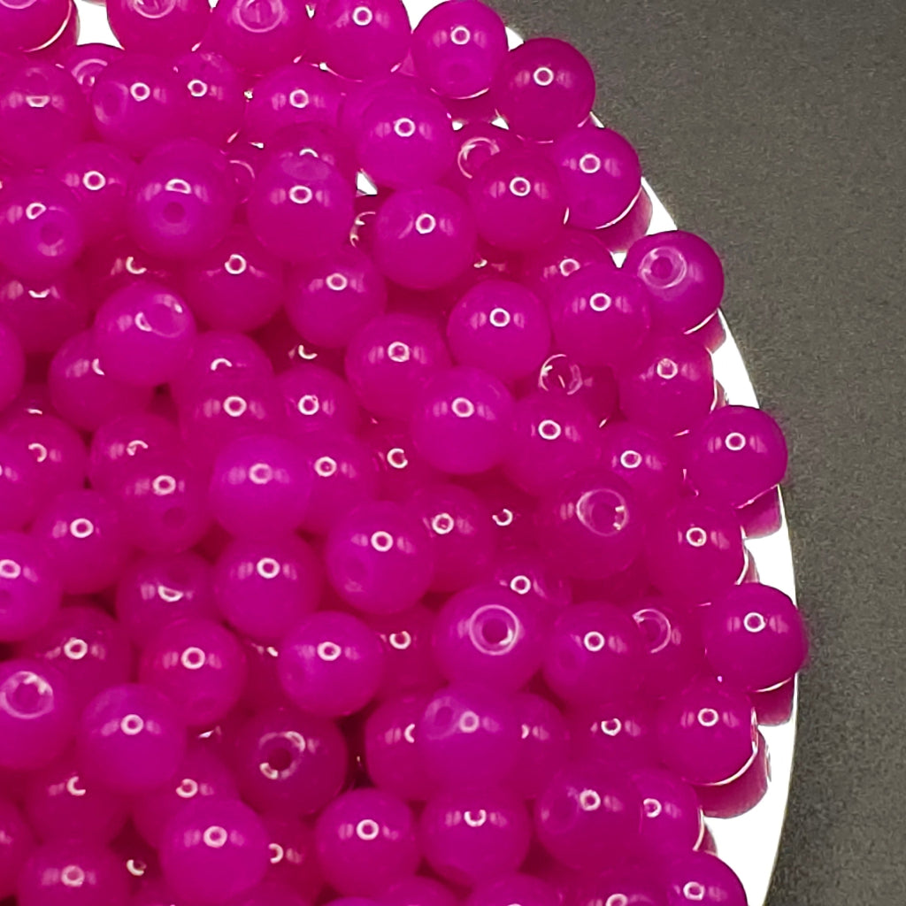 A pile of bright magenta pink translucent round beads with hollow centers, resting on a white plate against a dark gray background.