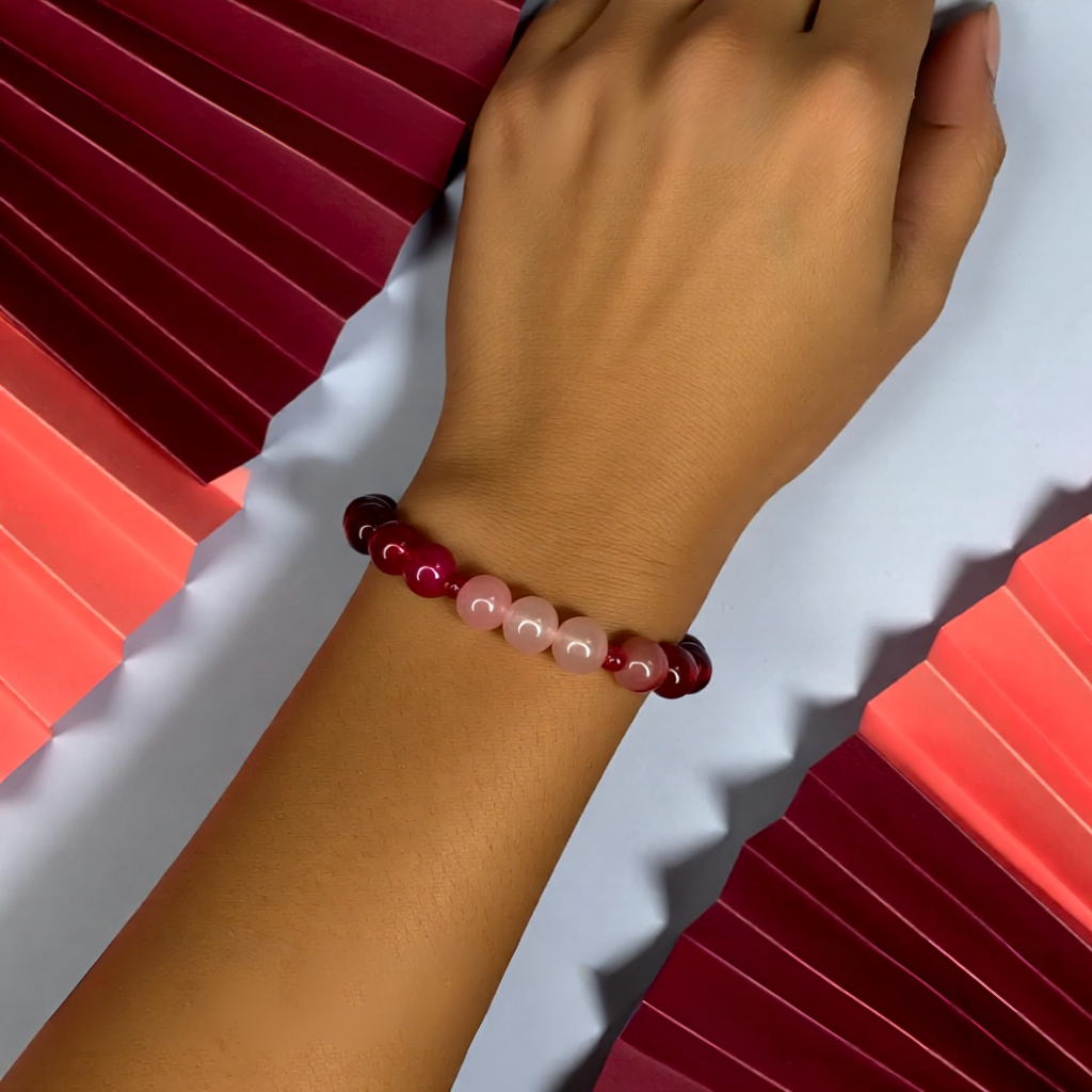 Hand wearing a beaded bracelet with red and pink stones against a white background
